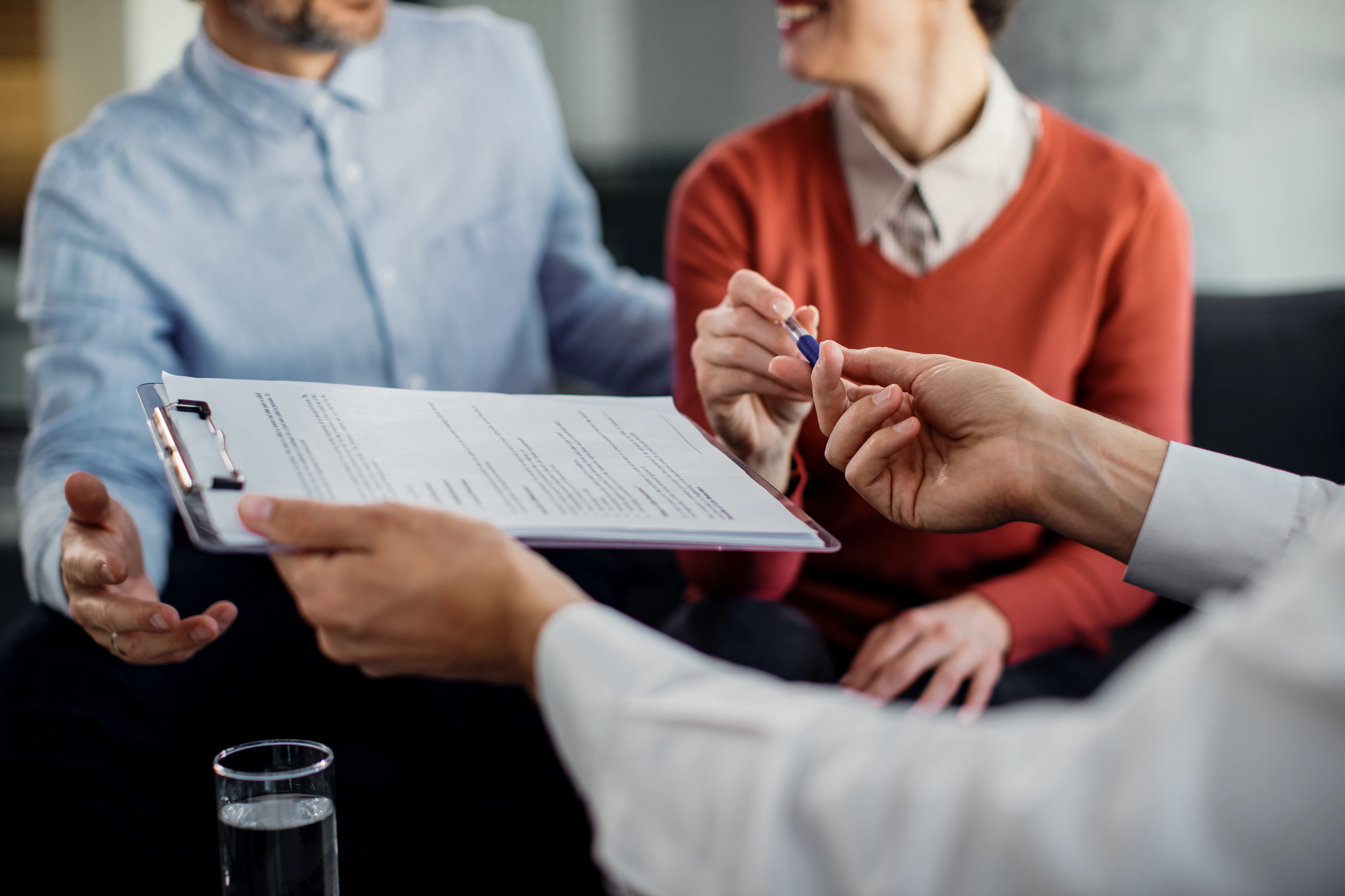 Clients grabbing pen from broker to sign private insurance paperwork