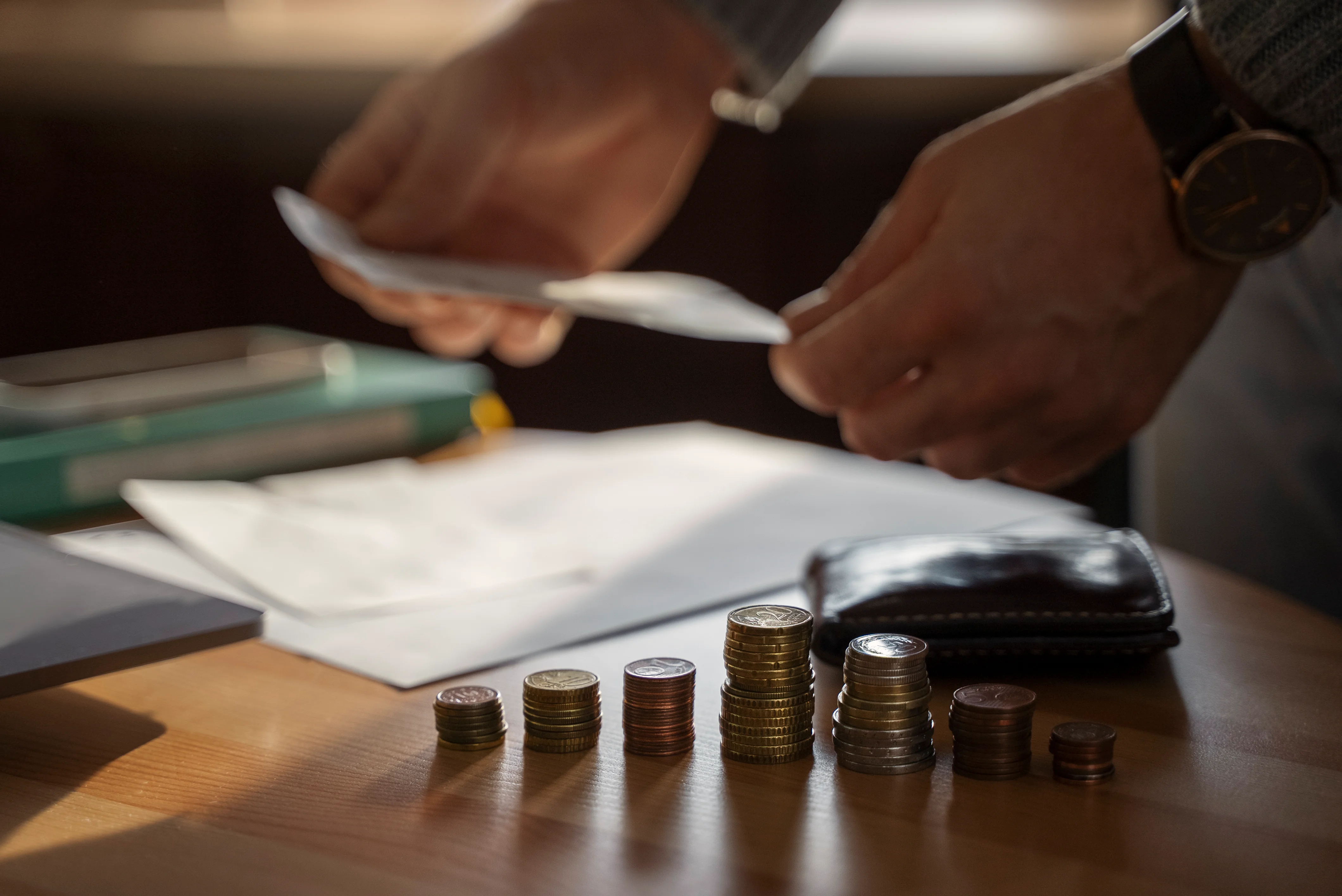 Close up of coins stacked in from of man analyzing expenses