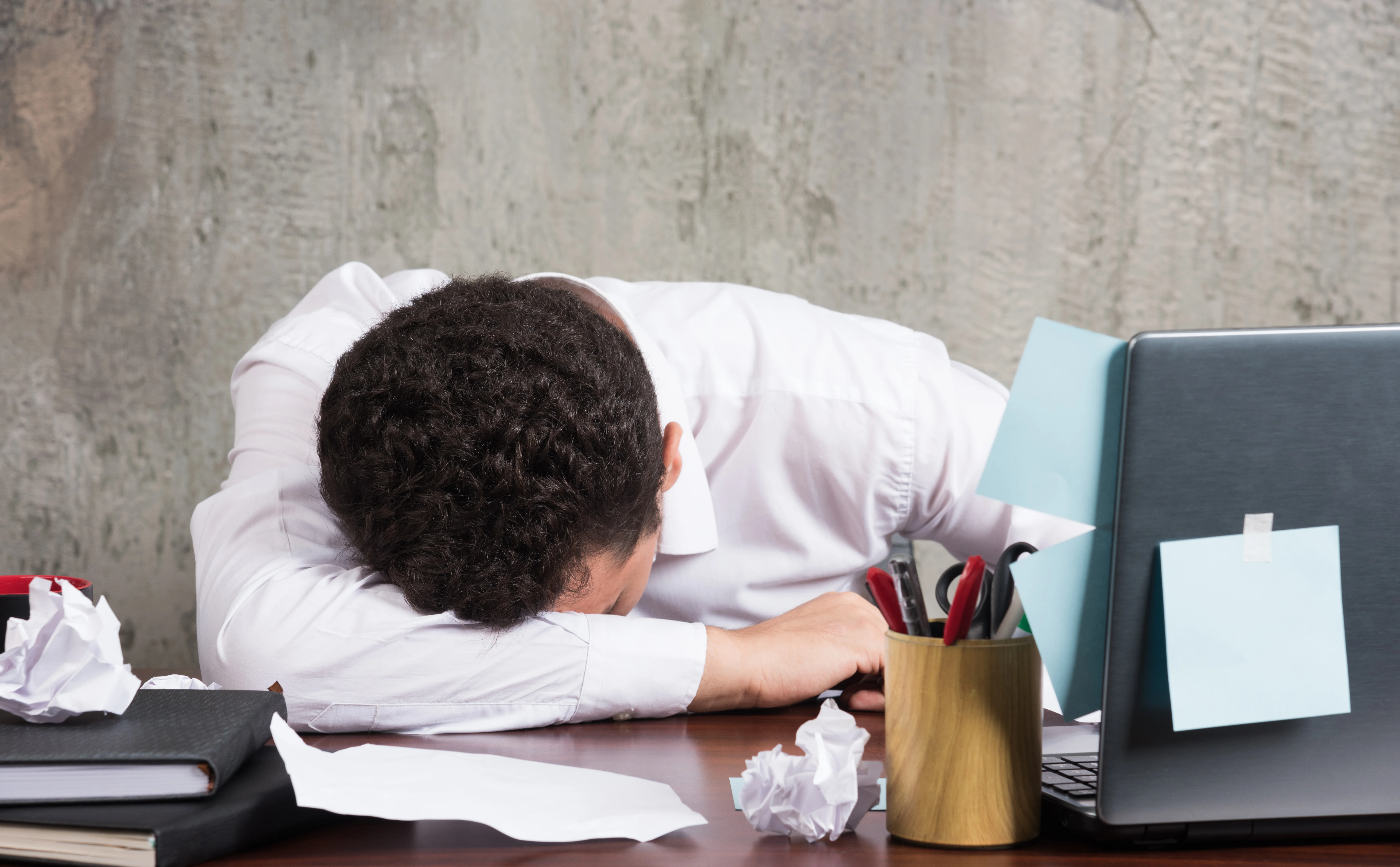 exhausted office worker with head down on desk next to laptop